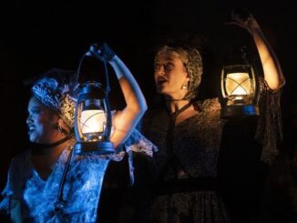 Two of the muses from "Hadestown" hold up lanterns.