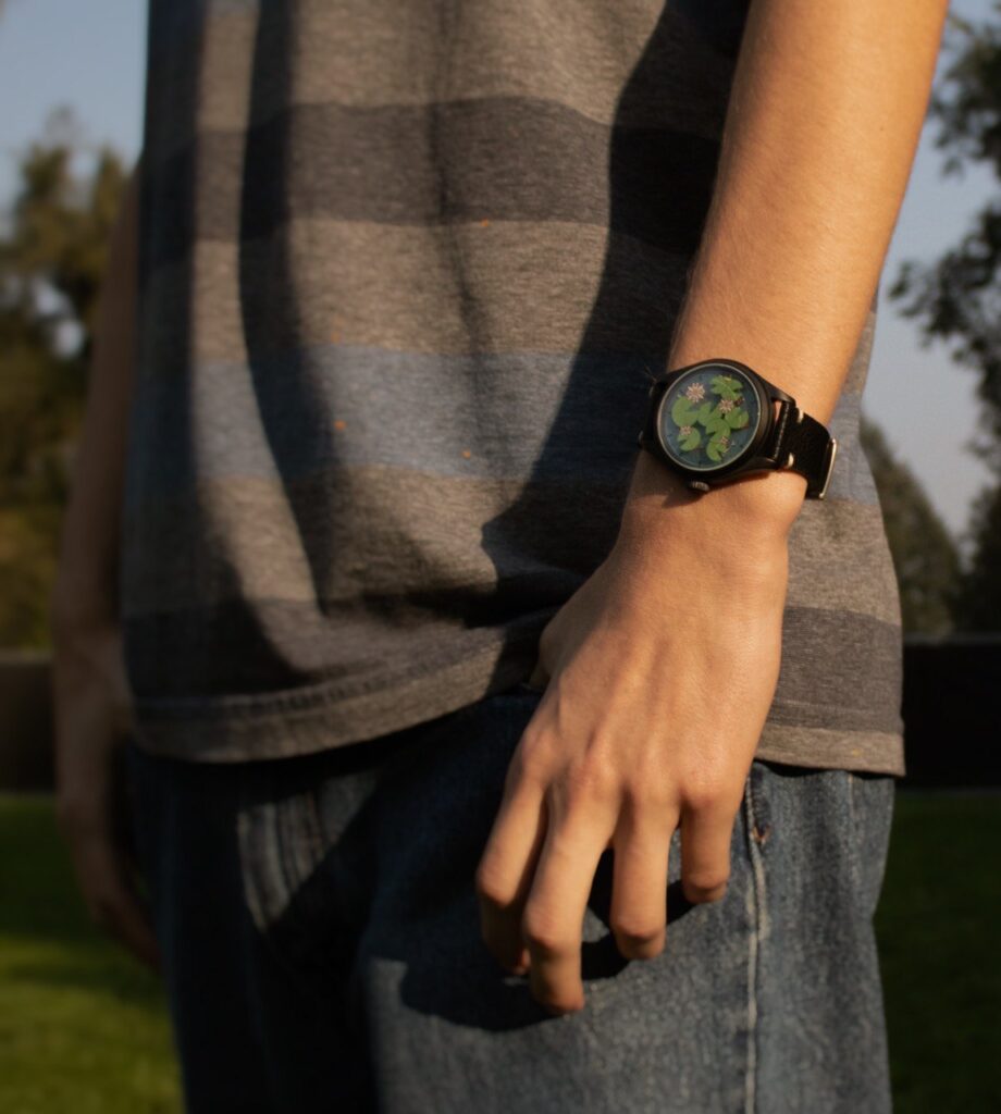 Photo of a man wearing a watch with lily pads, flowers, and fish on its face.