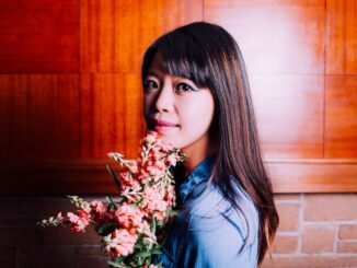 Image of Jane Wong staring at camera, holding a bouquet of flowers. brick background