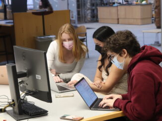A photo of 3 students with masks on looking at laptops and studying