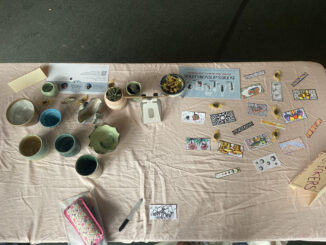 Photo of an assortment of handmade stickers, small thrown pottery pieces, and other ephemera seen from above spread out on a table