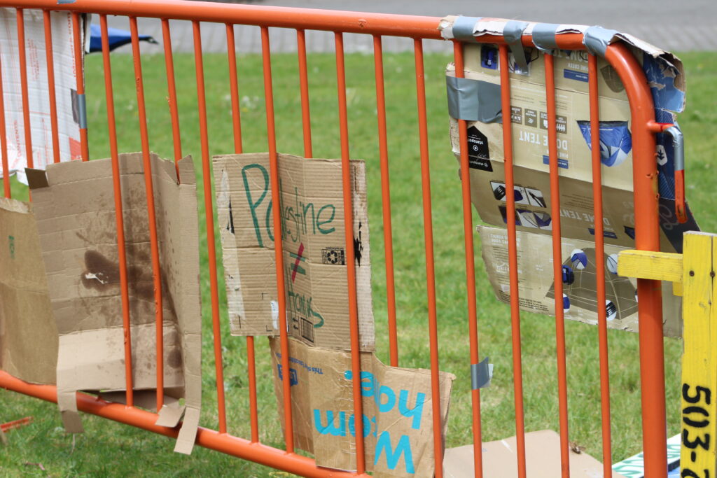 A cardboard sign woven through a barricade on site reads "Palestine ≠ Hamas."