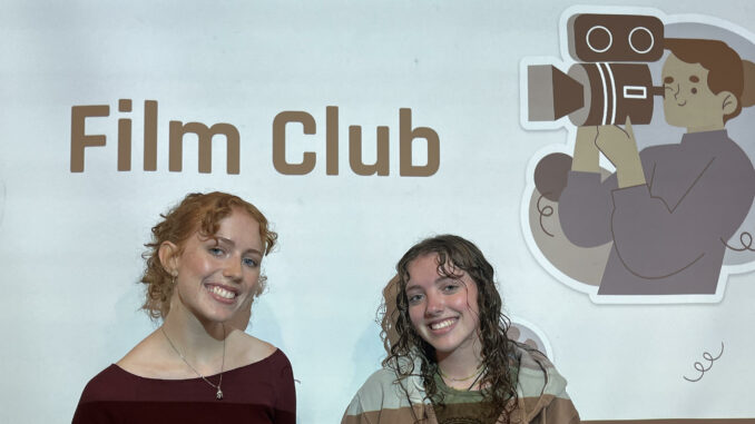 Maia Kesler and Grace Kelley pose with film club presentation behind them