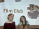 Maia Kesler and Grace Kelley pose with film club presentation behind them